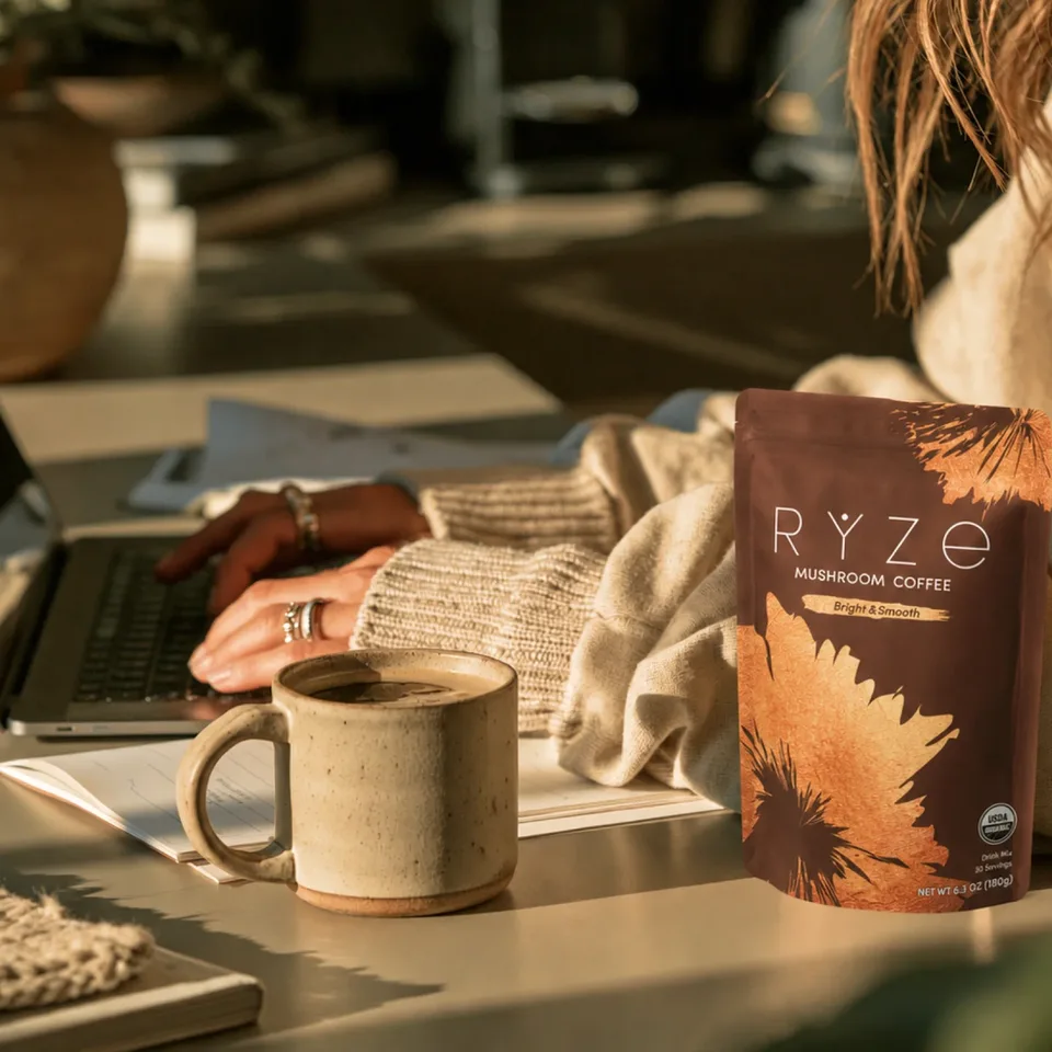 Working at a laptop beside a mug of RYZE mushroom coffee and the bag