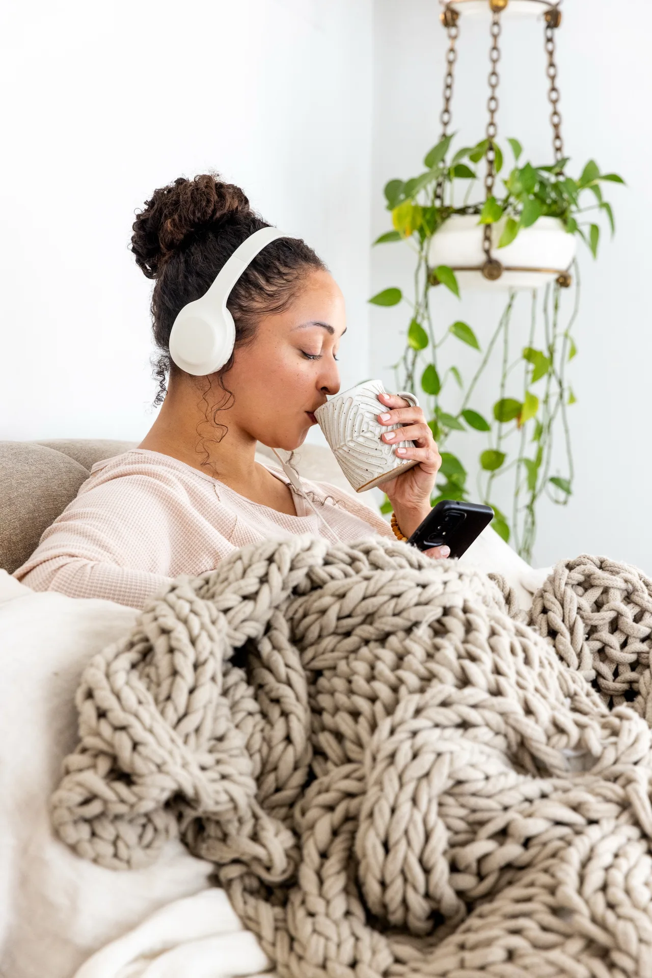 Woman wrapped in a blanket with headphones on, drinking RYZE mushroom coffee