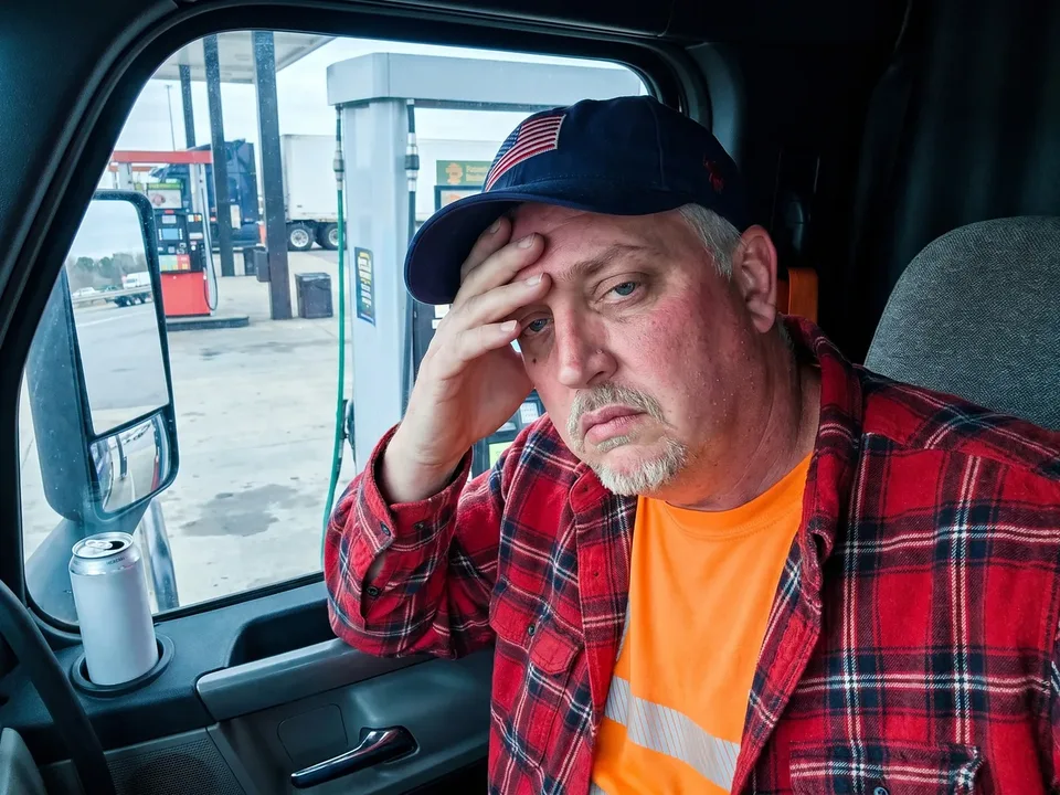 The truck driver from the ad slumped in his parked cab beside a generic energy-drink can during a long afternoon haul.