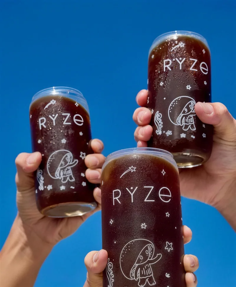 Three hands toasting iced RYZE coffees against a blue sky