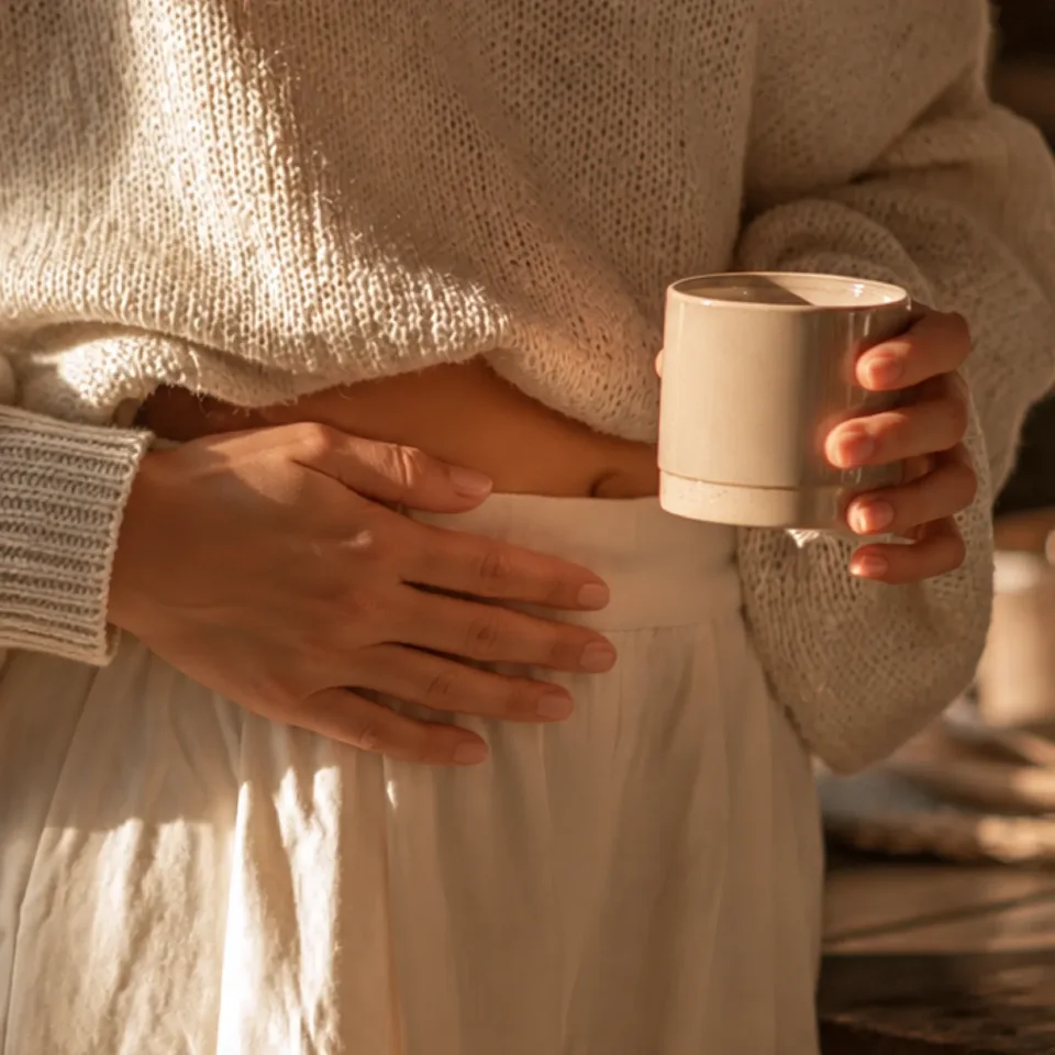 One hand resting on the stomach, the other holding a mug of RYZE mushroom coffee
