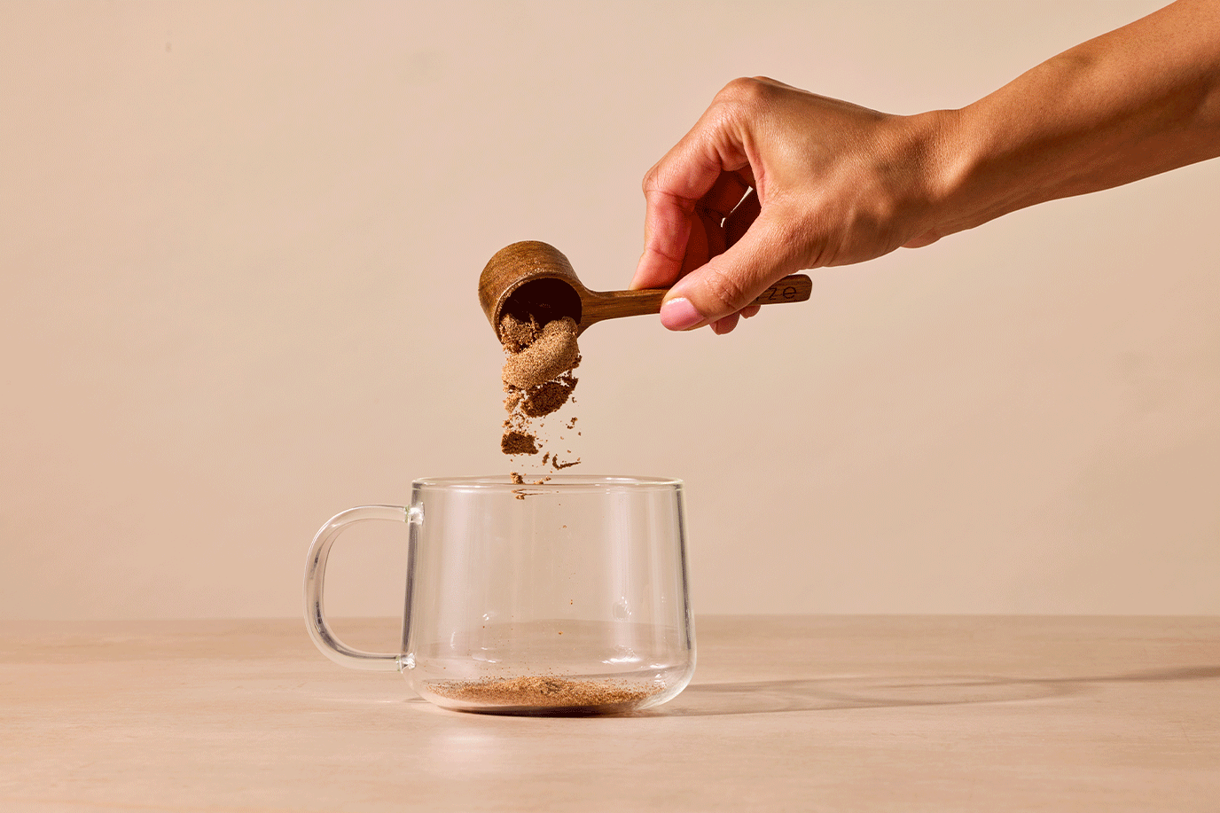 A wooden scoop pouring RYZE Mushroom Coffee powder into a clear glass mug, then water being added and stirred