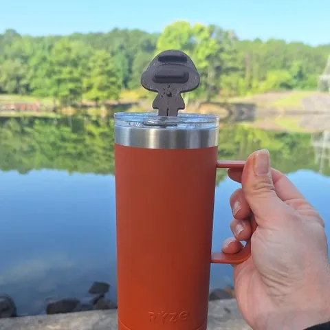 An orange RYZE tumbler on the rocks beside a fishing rod