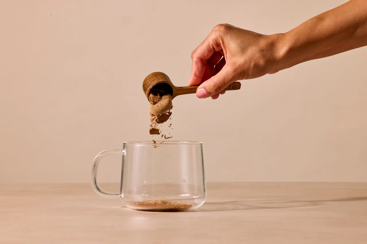 A wooden scoop pouring RYZE mushroom coffee into a glass mug