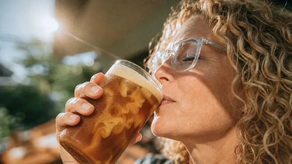 Woman sipping an iced RYZE Mushroom Coffee in the morning sun