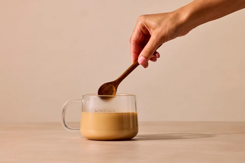A scoop of RYZE mushroom coffee powder being stirred into a mug