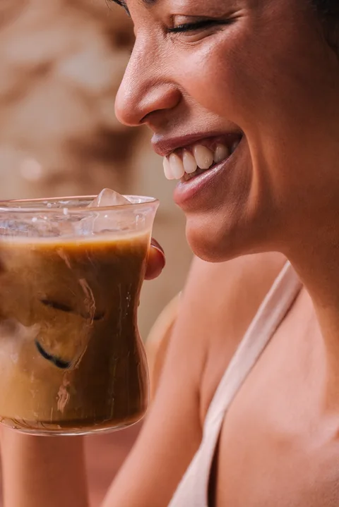 Smiling woman holding an iced RYZE mushroom coffee