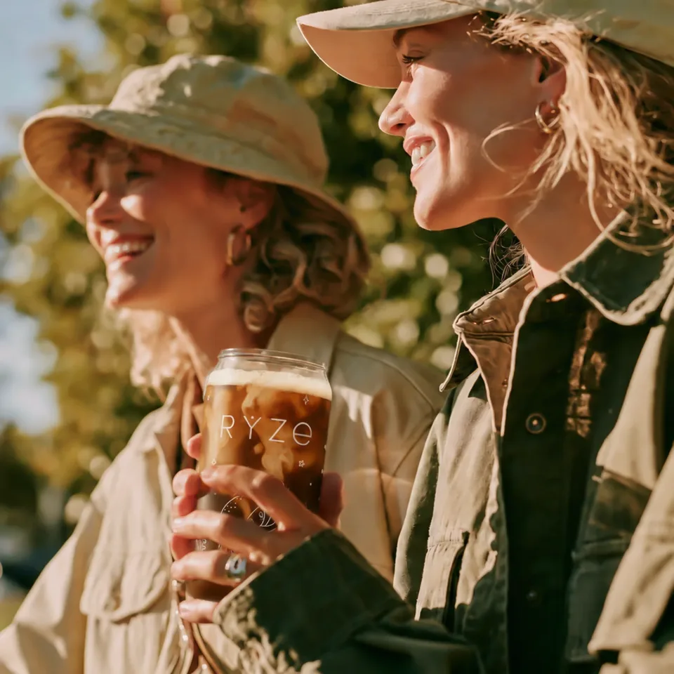 Two friends outdoors in the sun sharing an iced RYZE mushroom coffee