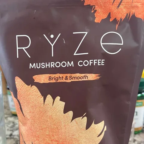 An orange RYZE tumbler on the rocks beside a fishing rod